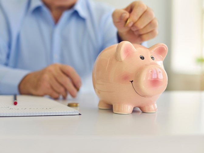 man puts money into piggy bank representing the act of saving for retirement