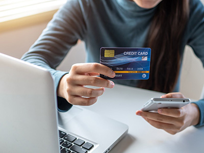 Person sitting at a desk with a laptop holding a phone and credit card