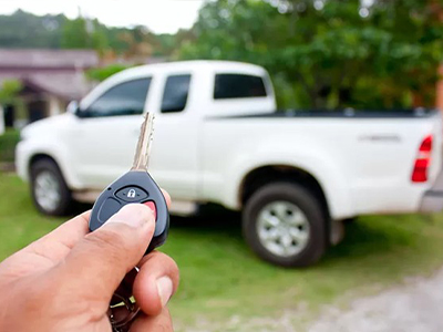 hand holding key fob in foreground and white pickup in background