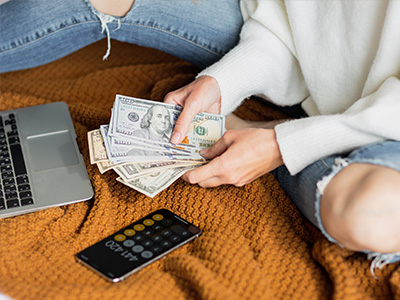 Young woman holding cash. Person counting money at home on bed.