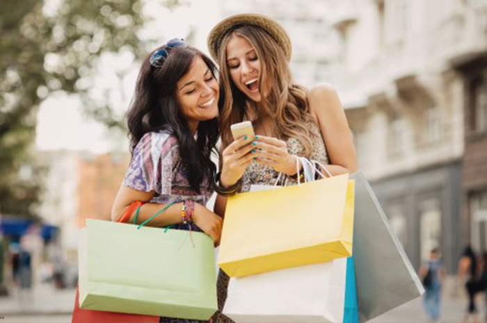 two women carrying shopping bags and shopping smart by checking deals before making a purchase