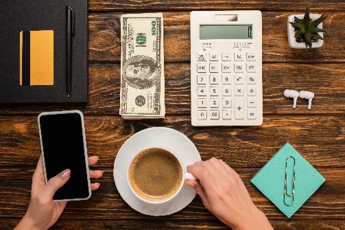 cropped view of a woman holding smartphone and coffee cup near dollar banknotes, calculator