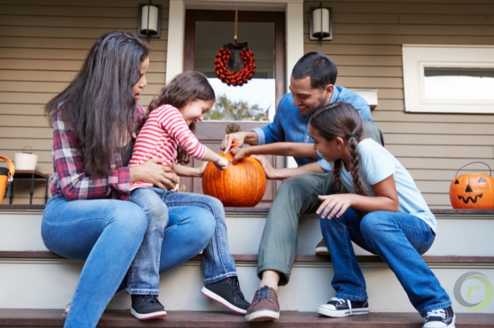 a family sits on the porch steps carving a pumpkin together