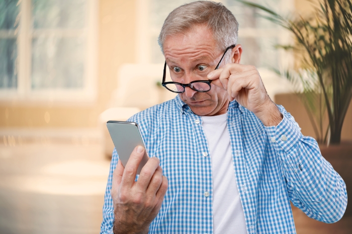 elderly man looks over his glasses at his phone