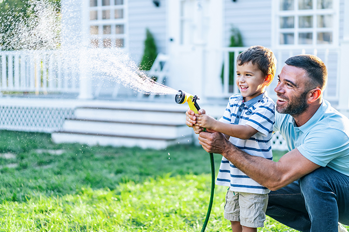 Family Cooking father helping young son water the grass in backyard of their home