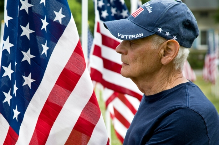 man wearing Veteran cap standing by U.S. flag