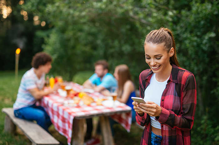 a woman smiles while looking at her phone during a backyard picnic